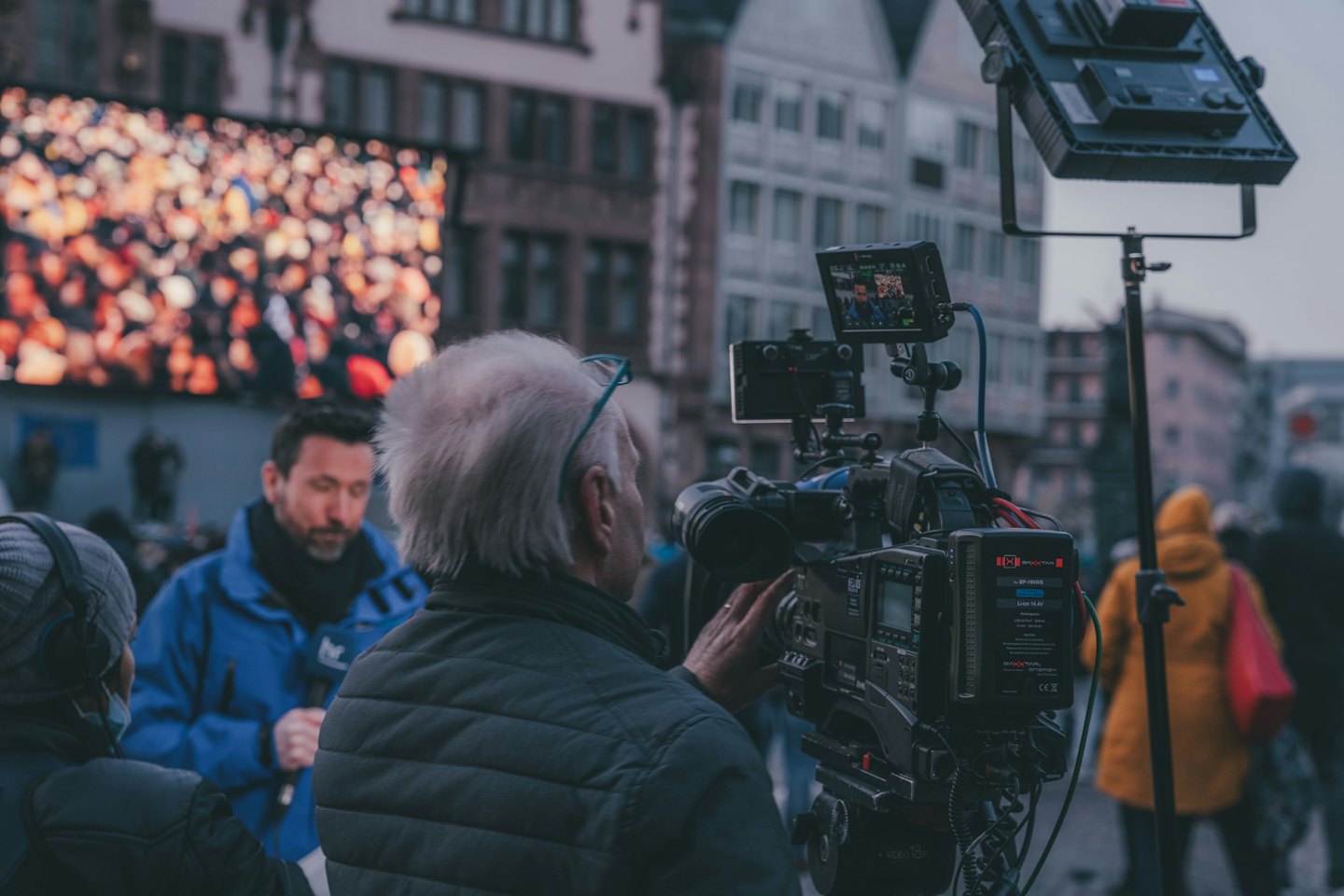 Camera operator films a reporter at an outdoor urban event.