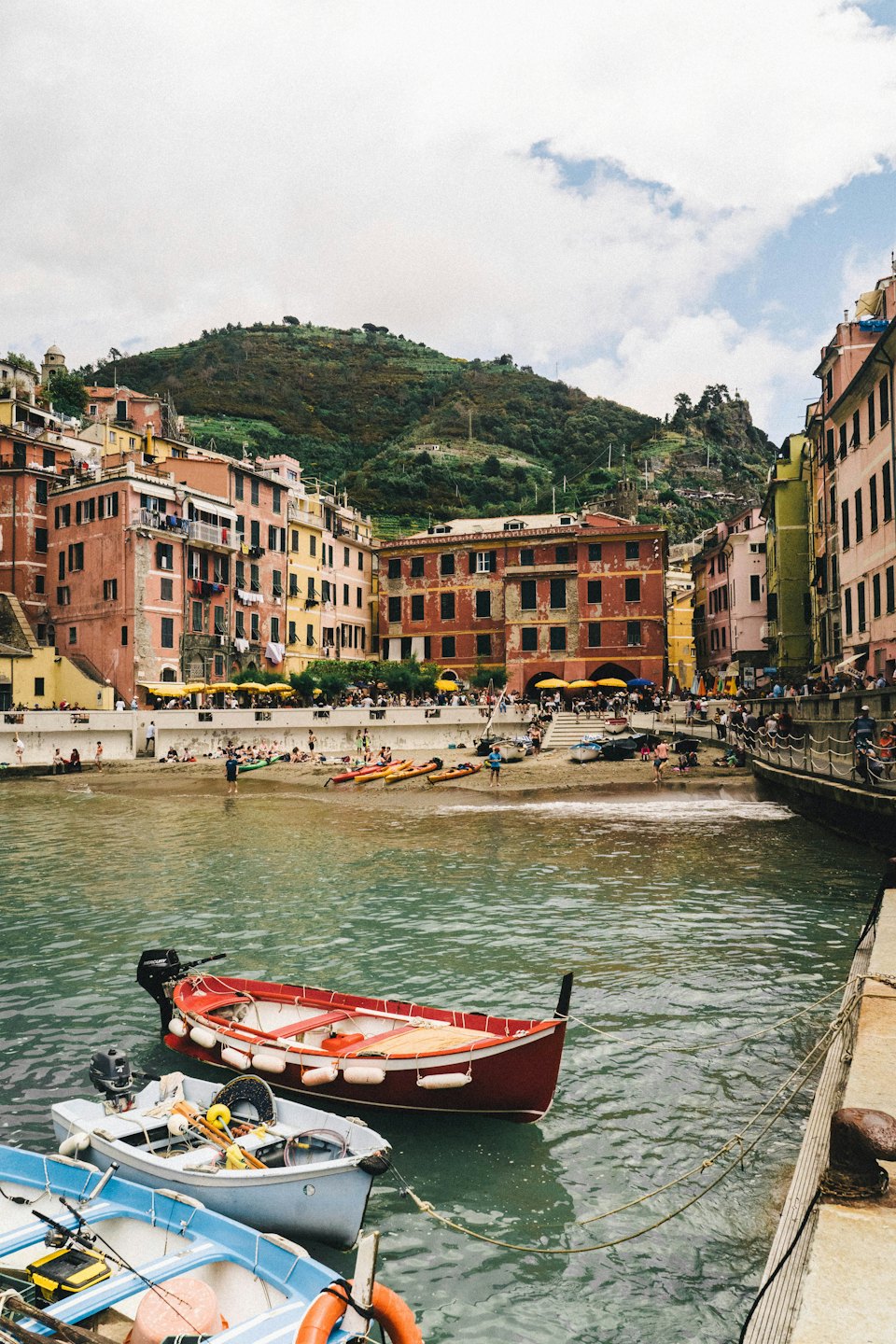 Colorful seaside village buildings sit along a busy beach and harbor.